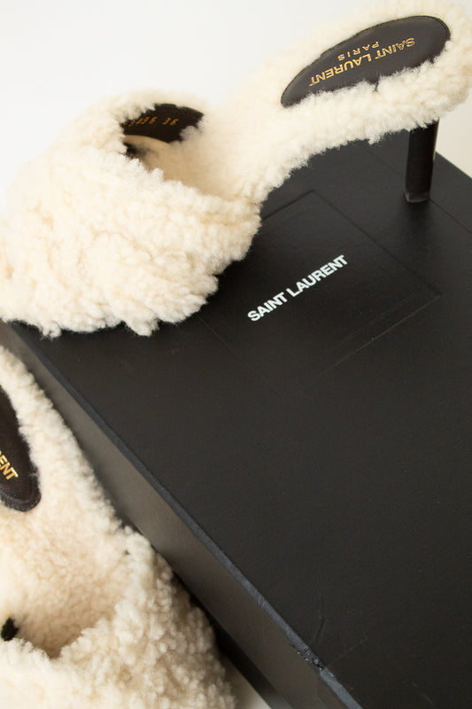 Saint Laurent fluffy cream shearling slide heel resting on a black branded shoebox against a clean white background.