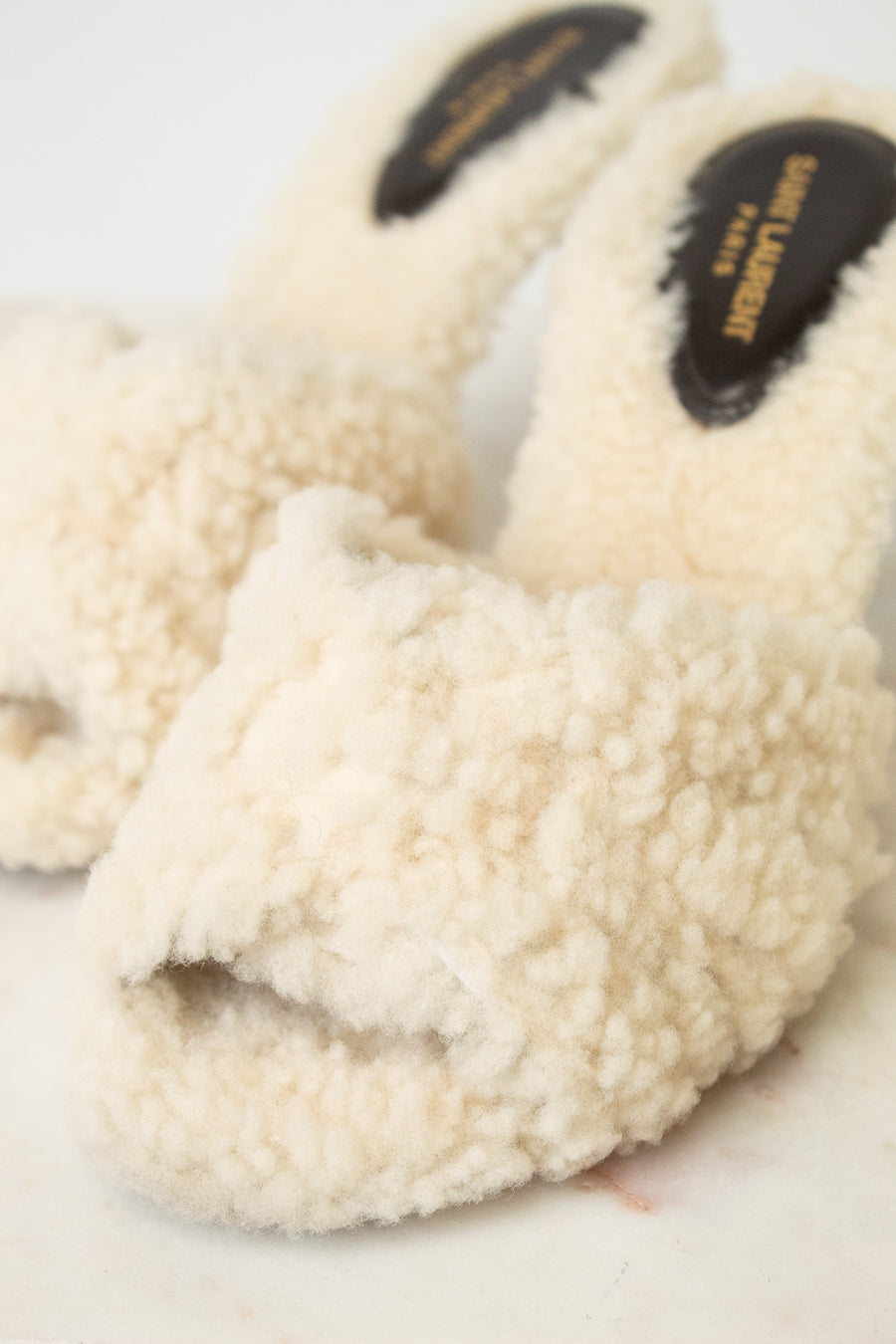 Cream shearling slide heel with black insole labels reading 'SAINT LAURENT PARIS'.