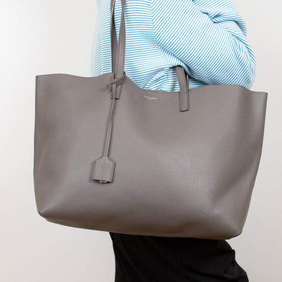 Person holding a large gray tote bag against a plain background
