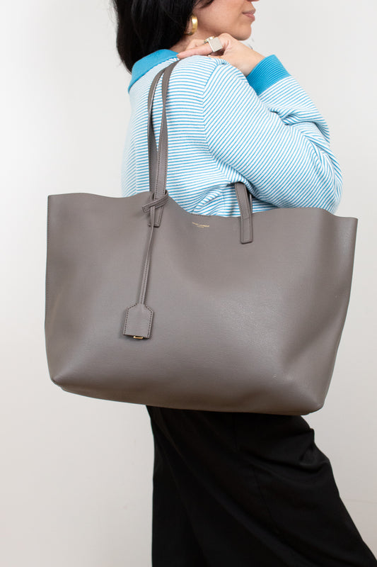 Person holding a large gray tote bag against a plain background