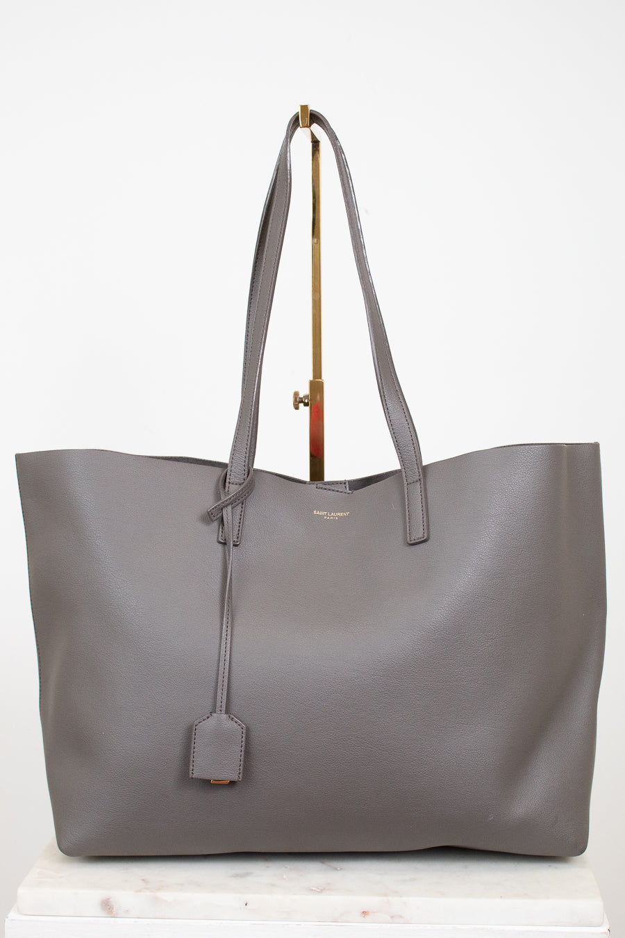 Gray tote bag with a "Saint Laurent" brand tag on a white background