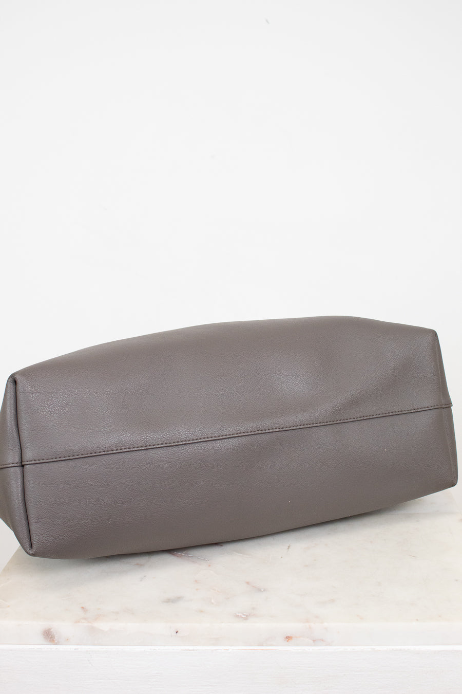 Gray leather bag on a white marble surface with a white background