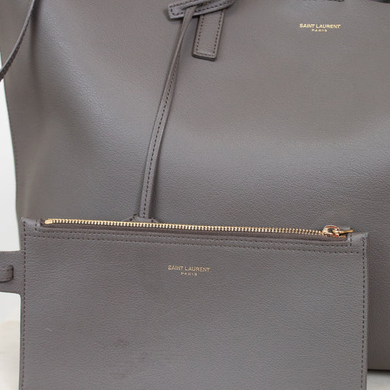 Gray handbag with small gray pouch with a visible "Saint Laurent" brand logo on a light background