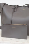 Gray handbag with small gray pouch with a visible "Saint Laurent" brand logo on a light background