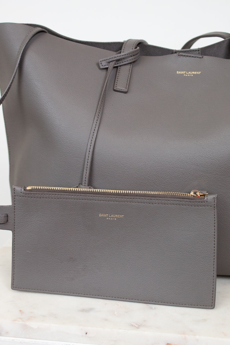 Gray handbag with small gray pouch with a visible "Saint Laurent" brand logo on a light background