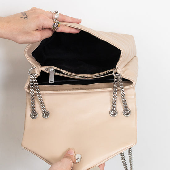 A beige leather shoulder bag with silver chain details and a black interior, held open by two hands against a plain white background.