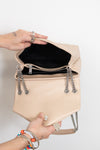 A beige leather shoulder bag with silver chain details and a black interior, held open by two hands against a plain white background.