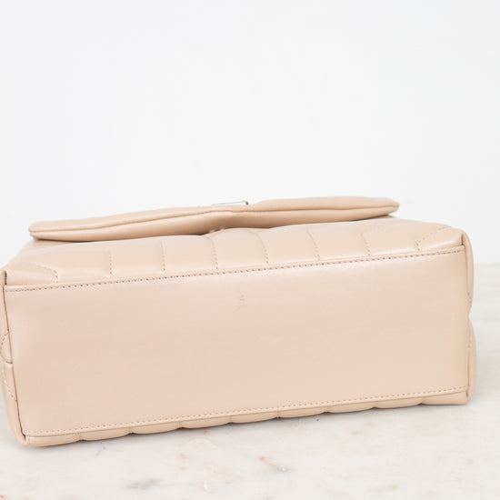 A light beige leather bag with a quilted top flap, resting on a white marble surface against a white background.