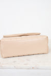 A light beige leather bag with a quilted top flap, resting on a white marble surface against a white background.