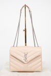 A light beige quilted leather shoulder bag with a silver-tone YSL monogram clasp, displayed on a gold stand with a white background.