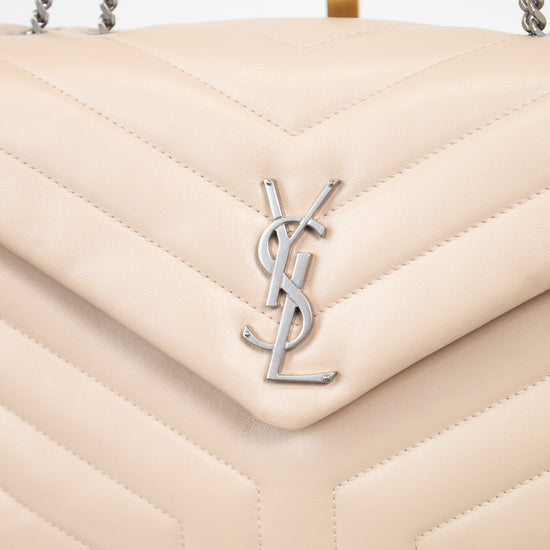 A close-up of a quilted cream-colored leather handbag with a silver-tone YSL logo on the front flap and silver chain straps, resting on a marble surface.