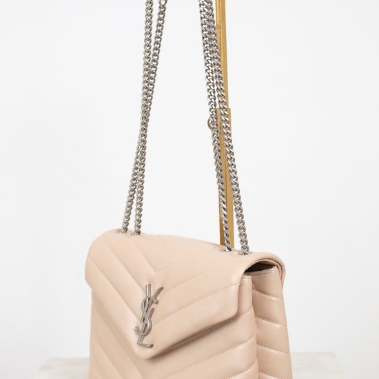 A light beige quilted leather shoulder bag with a silver-tone chain strap and a silver-tone YSL logo on the front, displayed on a marble surface against a white background.