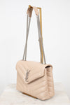 A light beige quilted leather shoulder bag with a silver-tone chain strap and a silver-tone YSL logo on the front, displayed on a marble surface against a white background.