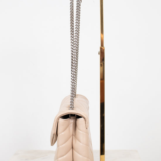A light beige quilted leather shoulder bag with a silver chain strap, displayed on a gold metal stand against a white background.