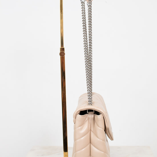 A light beige quilted leather shoulder bag with a silver chain strap, displayed on a gold metal stand against a white background.