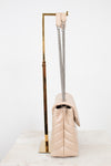 A light beige quilted leather shoulder bag with a silver chain strap, displayed on a gold metal stand against a white background.