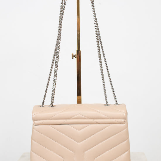 A light beige quilted leather shoulder bag with a geometric chevron pattern, featuring silver-tone chain straps and a gold-tone metal handle, displayed on a stand.