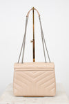 A light beige quilted leather shoulder bag with a geometric chevron pattern, featuring silver-tone chain straps and a gold-tone metal handle, displayed on a stand.