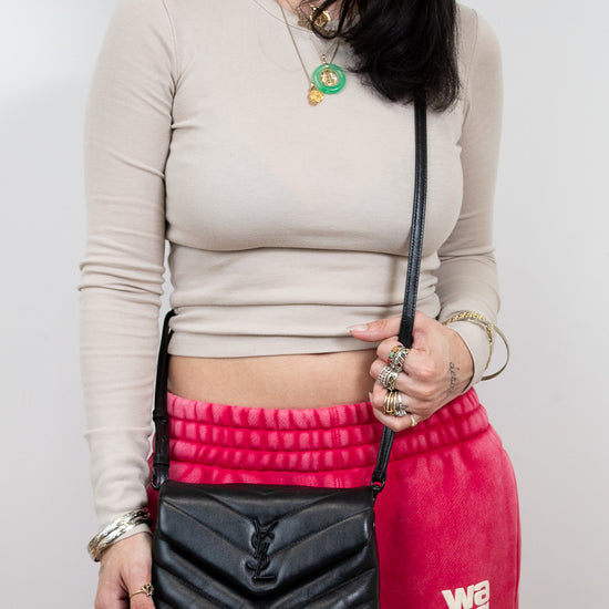 Woman holding a black handbag wearing a beige long-sleeve top and pink pants with 'Wang' text.