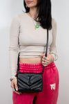 Woman holding a black handbag wearing a beige long-sleeve top and pink pants with 'Wang' text.