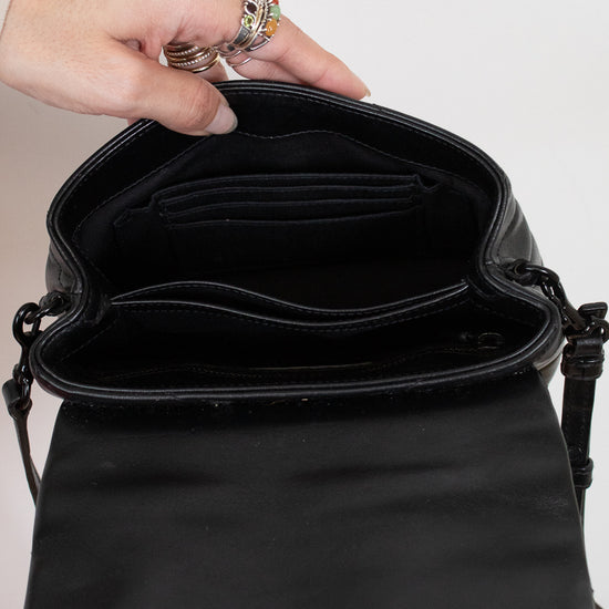 Black handbag held open by a hand with rings on a neutral background