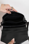 Black handbag held open by a hand with rings on a neutral background
