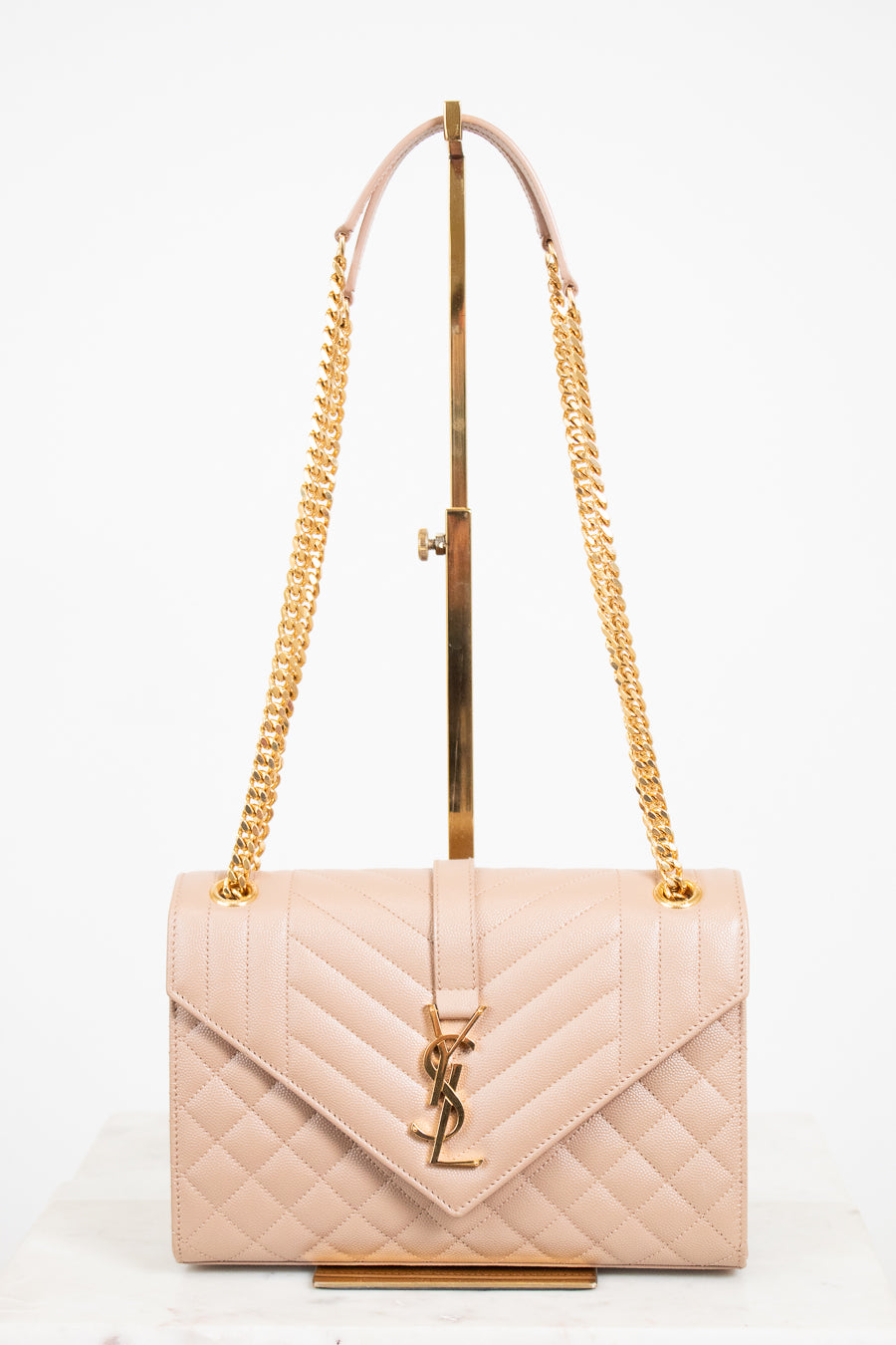 Beige quilted handbag with gold chain strap and logo on a white background