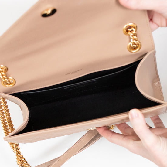Beige handbag with gold chain strap held by a hand on a white background