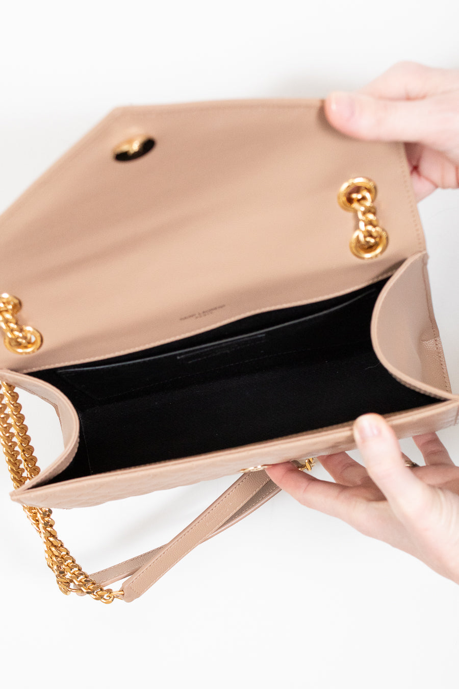 Beige handbag with gold chain strap held by a hand on a white background