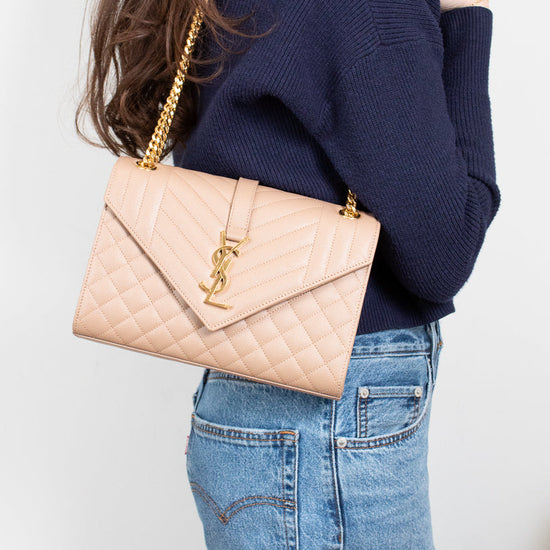 Person wearing a navy sweater and blue jeans with a beige quilted handbag on a plain background