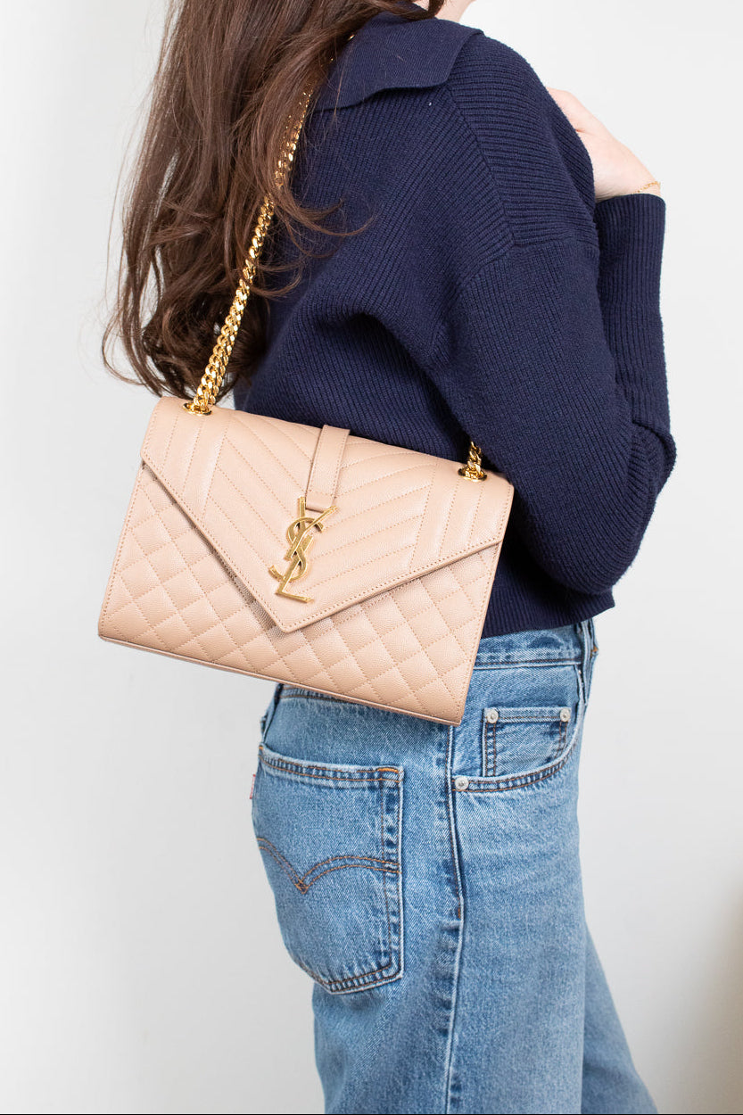 Person wearing a navy sweater and blue jeans with a beige quilted handbag on a plain background