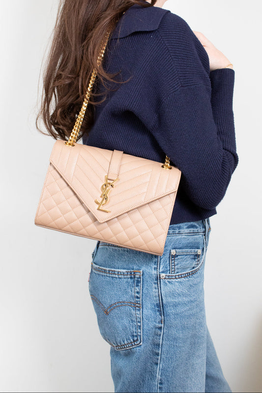 Person wearing a navy sweater and blue jeans with a beige quilted handbag on a plain background
