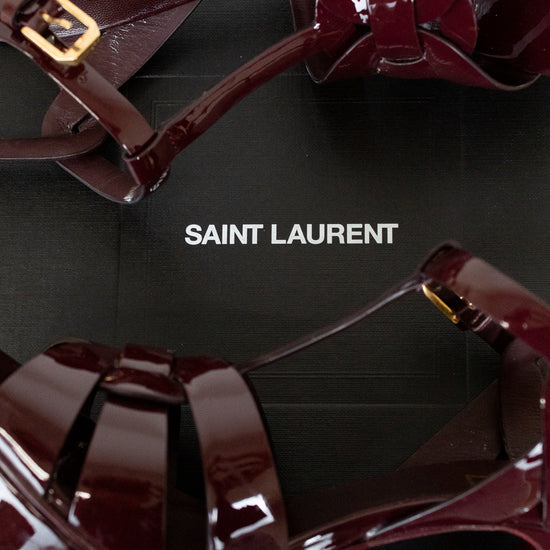 Shiny red high-heeled shoes with gold accents on a black background, featuring the Saint Laurent logo.