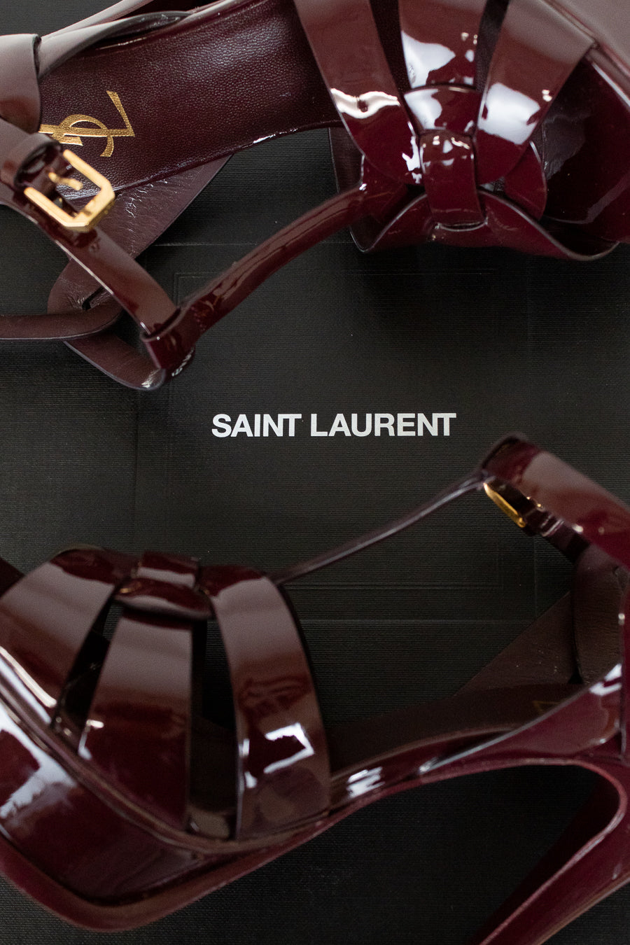 Shiny red high-heeled shoes with gold accents on a black background, featuring the Saint Laurent logo.