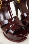 Shiny maroon high-heeled sandals with a bow detail on a light background