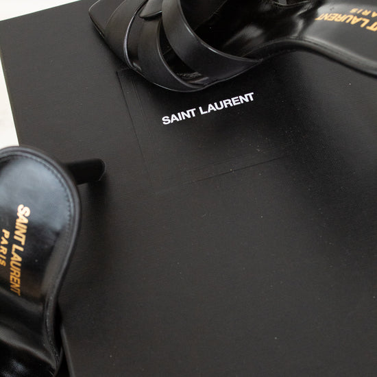 Black sandals and shoe box with 'Saint Laurent' logo on a black surface