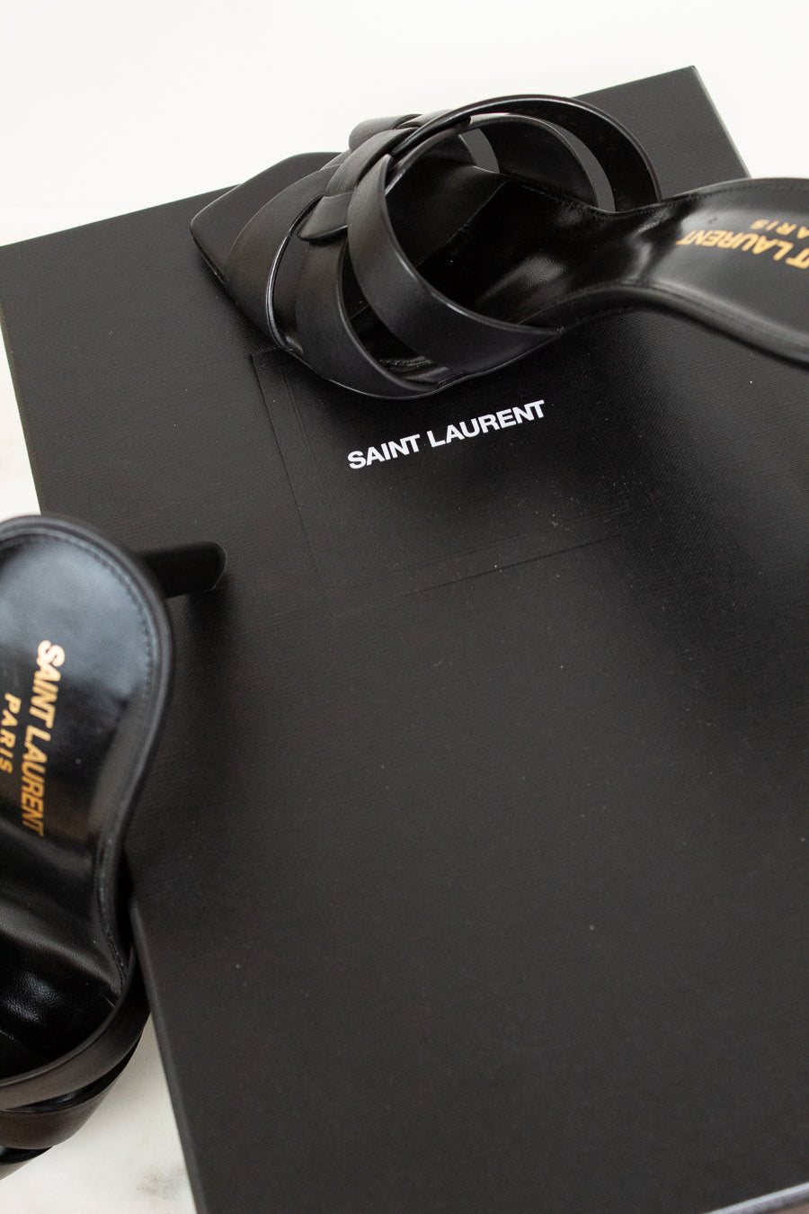 Black sandals and shoe box with 'Saint Laurent' logo on a black surface