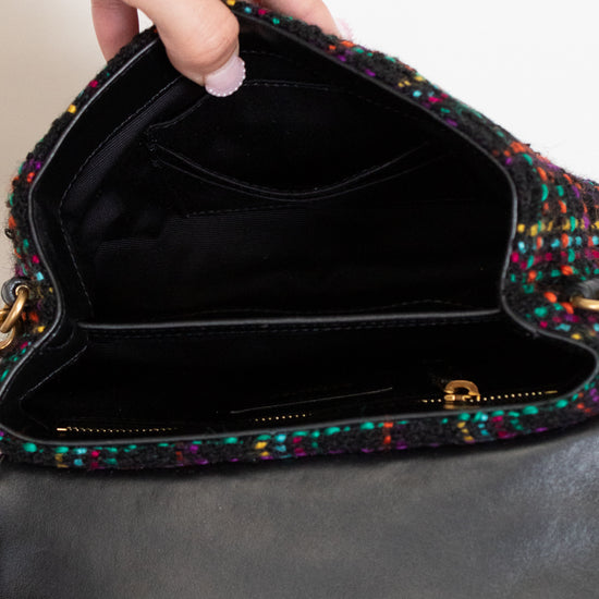 Multicolored textured handbag held by a hand with a ring, on a neutral background