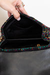 Multicolored textured handbag held by a hand with a ring, on a neutral background