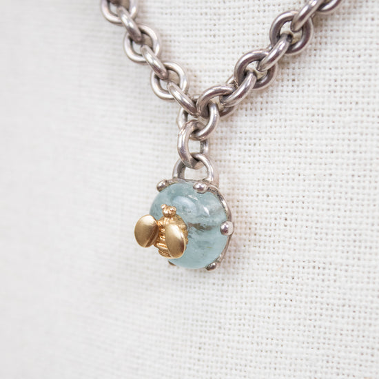 Necklace with a blue stone pendant and gold bee charm on a white background