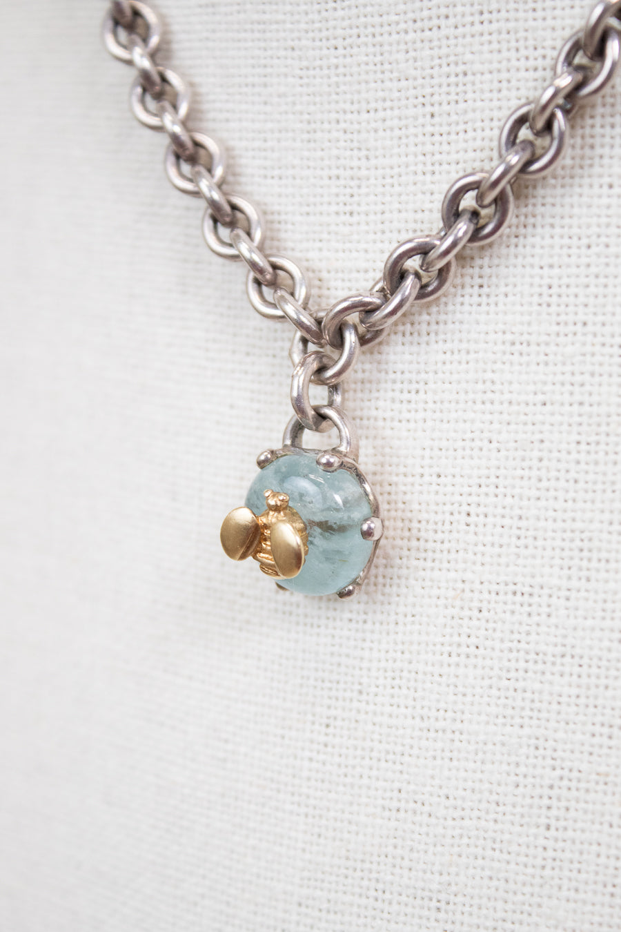 Necklace with a blue stone pendant and gold bee charm on a white background