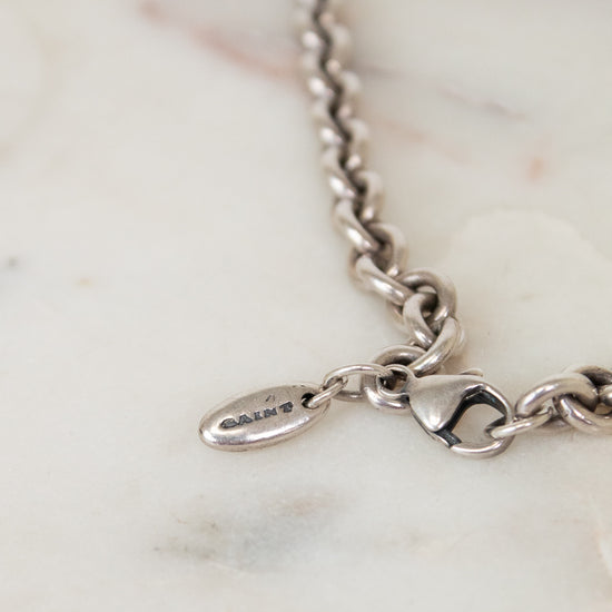 Silver bracelet with a oval-shaped logo charm on a marble surface