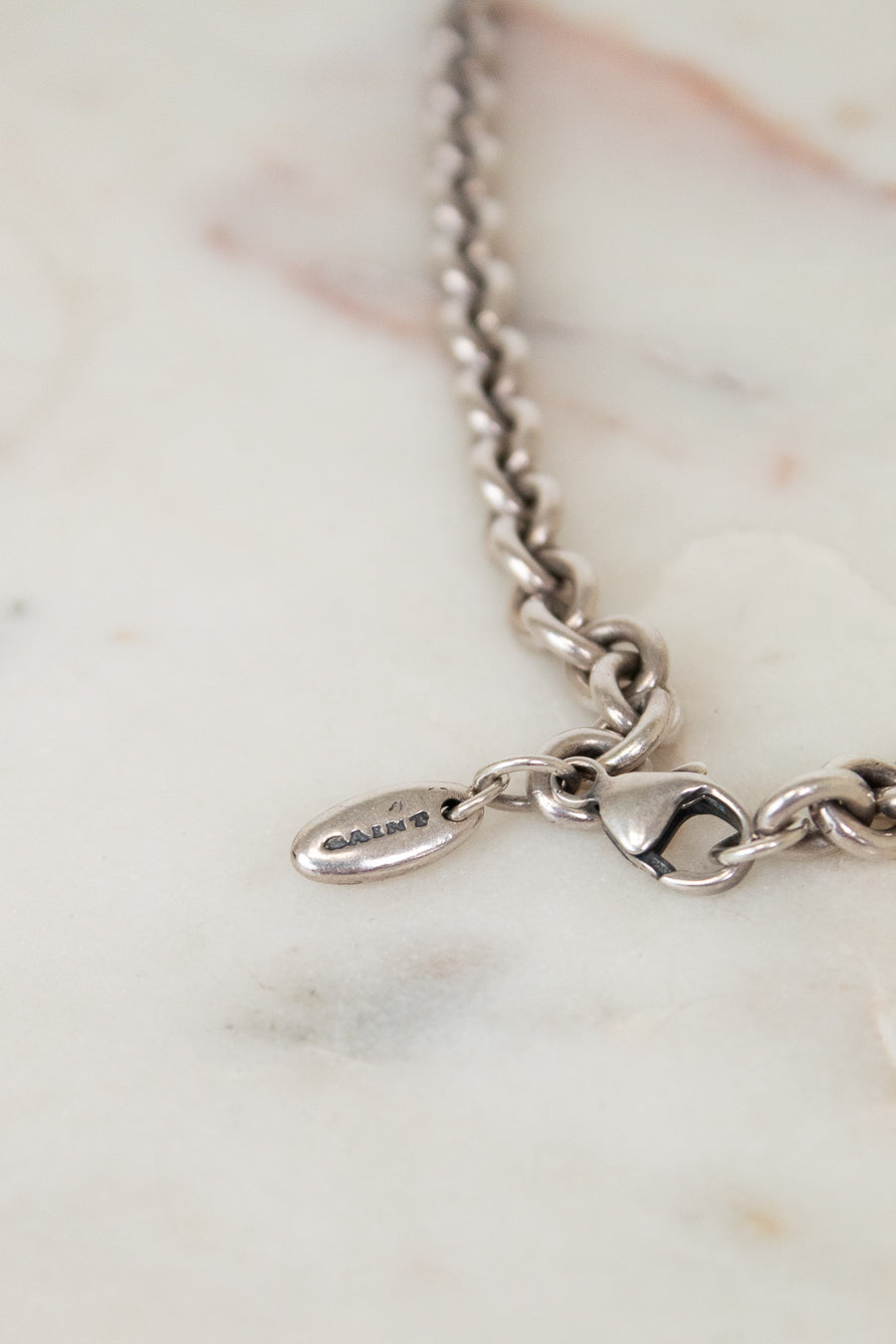 Silver bracelet with a oval-shaped logo charm on a marble surface