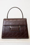A dark brown leather handbag with an embossed geometric circle pattern, featuring a top handle, a front flap pocket, and small gold-tone hardware, shown against a plain white background.