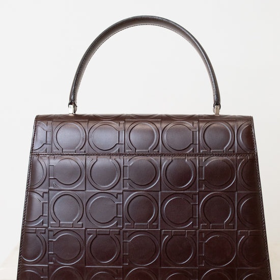 A dark brown leather handbag with a top handle, featuring an embossed geometric pattern of interlocking circles across the front, set against a plain white background.