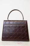 A dark brown leather handbag with a top handle, featuring an embossed geometric pattern of interlocking circles across the front, set against a plain white background.