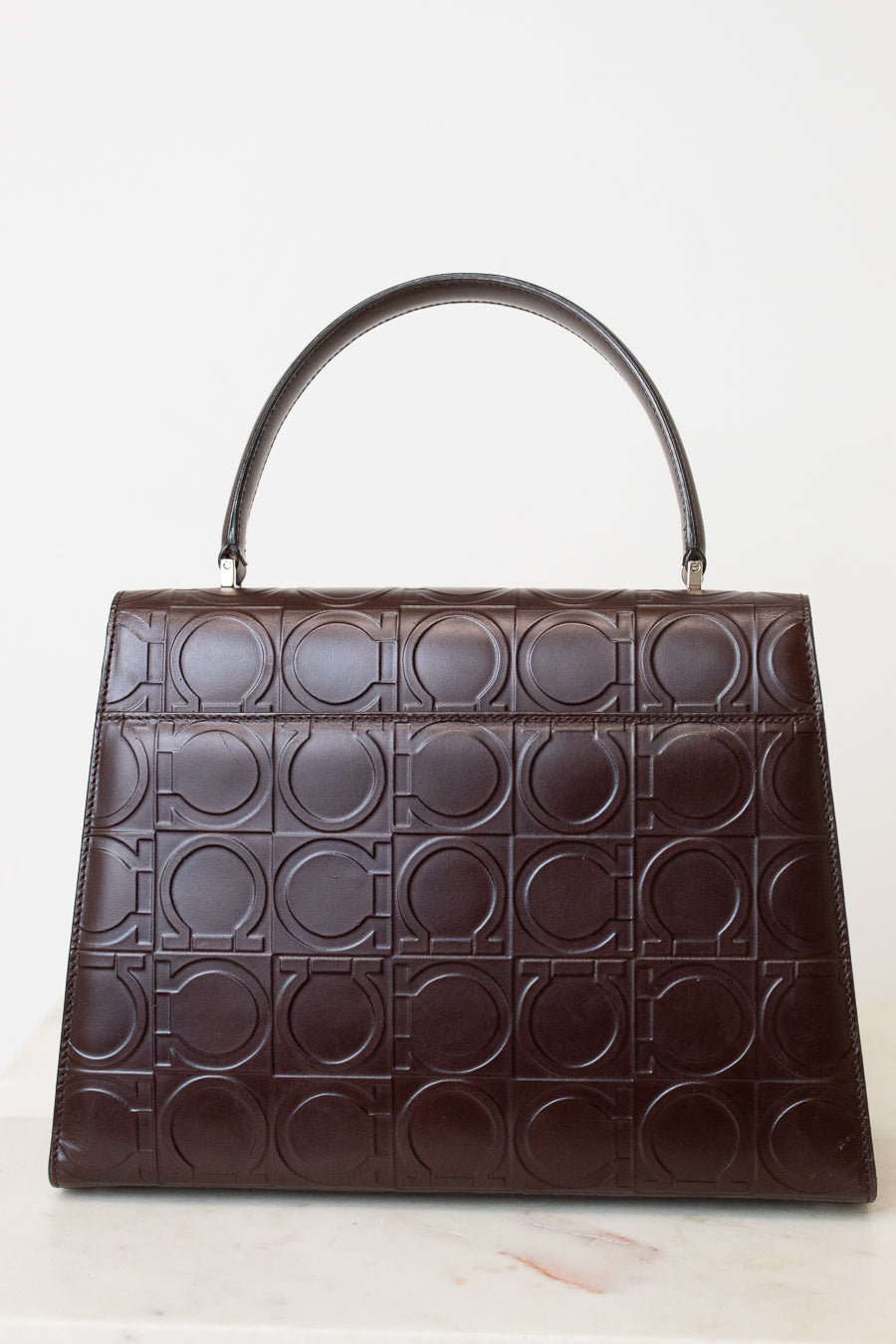 A dark brown leather handbag with a top handle, featuring an embossed geometric pattern of interlocking circles across the front, set against a plain white background.