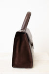 A dark brown handbag shown from a side profile view, featuring a dark brown suede-like interior and a textured dark brown exterior, set against a plain white background.