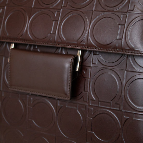 A close-up of a dark brown leather handbag featuring an embossed geometric circular pattern and a matching flap pocket with gold-tone hardware.