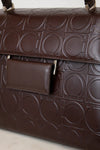 A close-up of a dark brown leather handbag featuring an embossed geometric circular pattern and a matching flap pocket with gold-tone hardware.